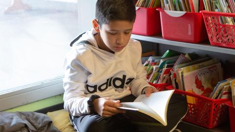 Elementary school aged boy reading a book beside classroom library bins