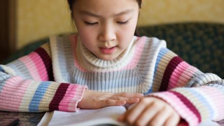 Closeup of elementary school girl in striped sweater reading a book